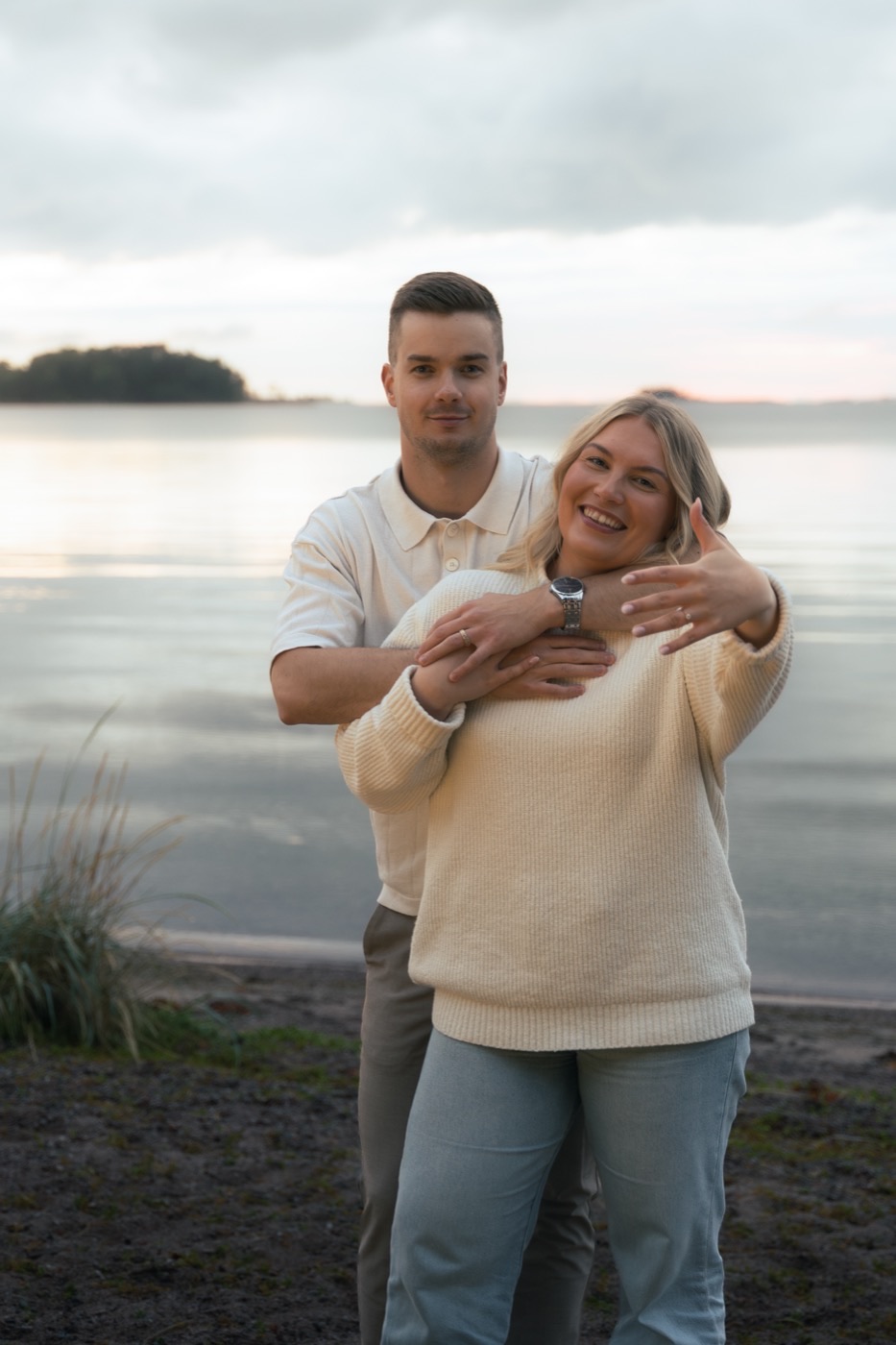 Nauravat kihlautuneet halaavat toisiaan järven rannalla